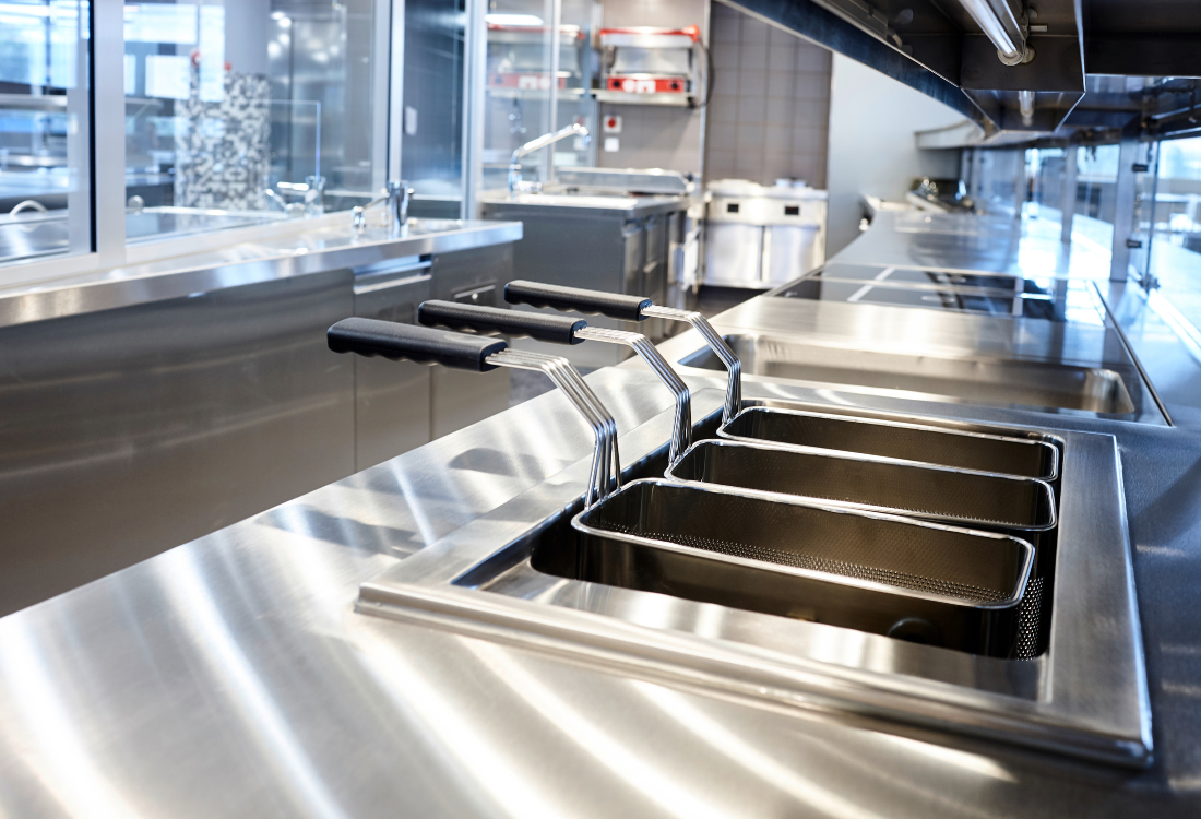 Empty commercial kitchen with stainless steel workstations and appliances, showcasing the different grades of stainless steel used in food preparation areas.
