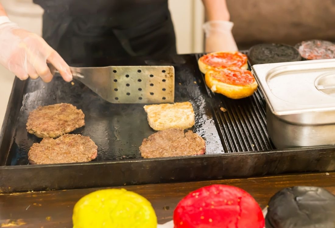 A commercial electric griddle being used to make burgers.