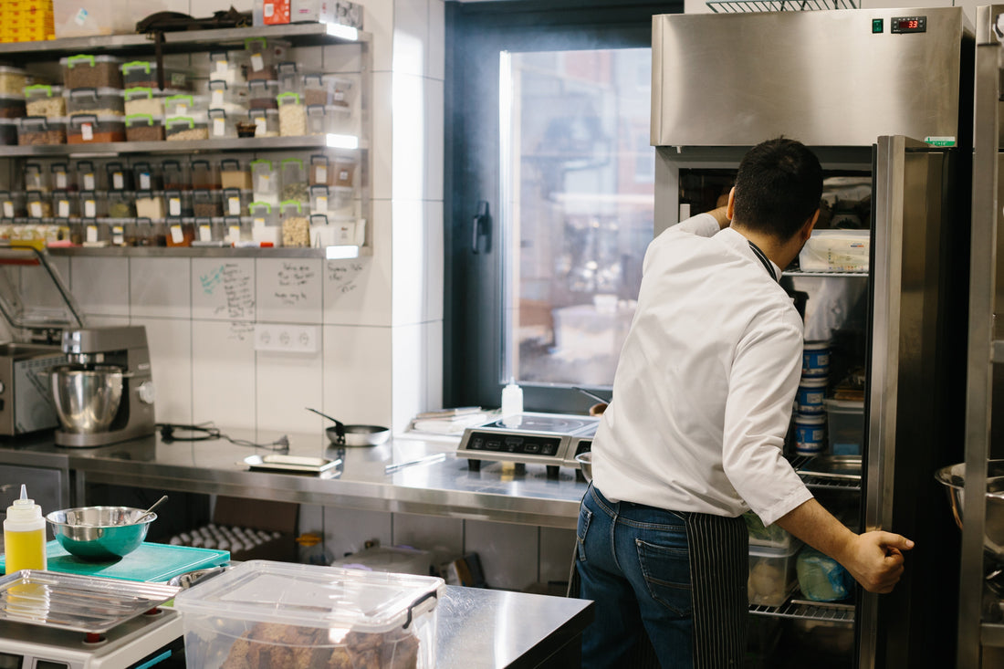 Chef organising ingredients in a commercial refrigeration unit to maintain food safety and reduce waste in a restaurant kitchen.