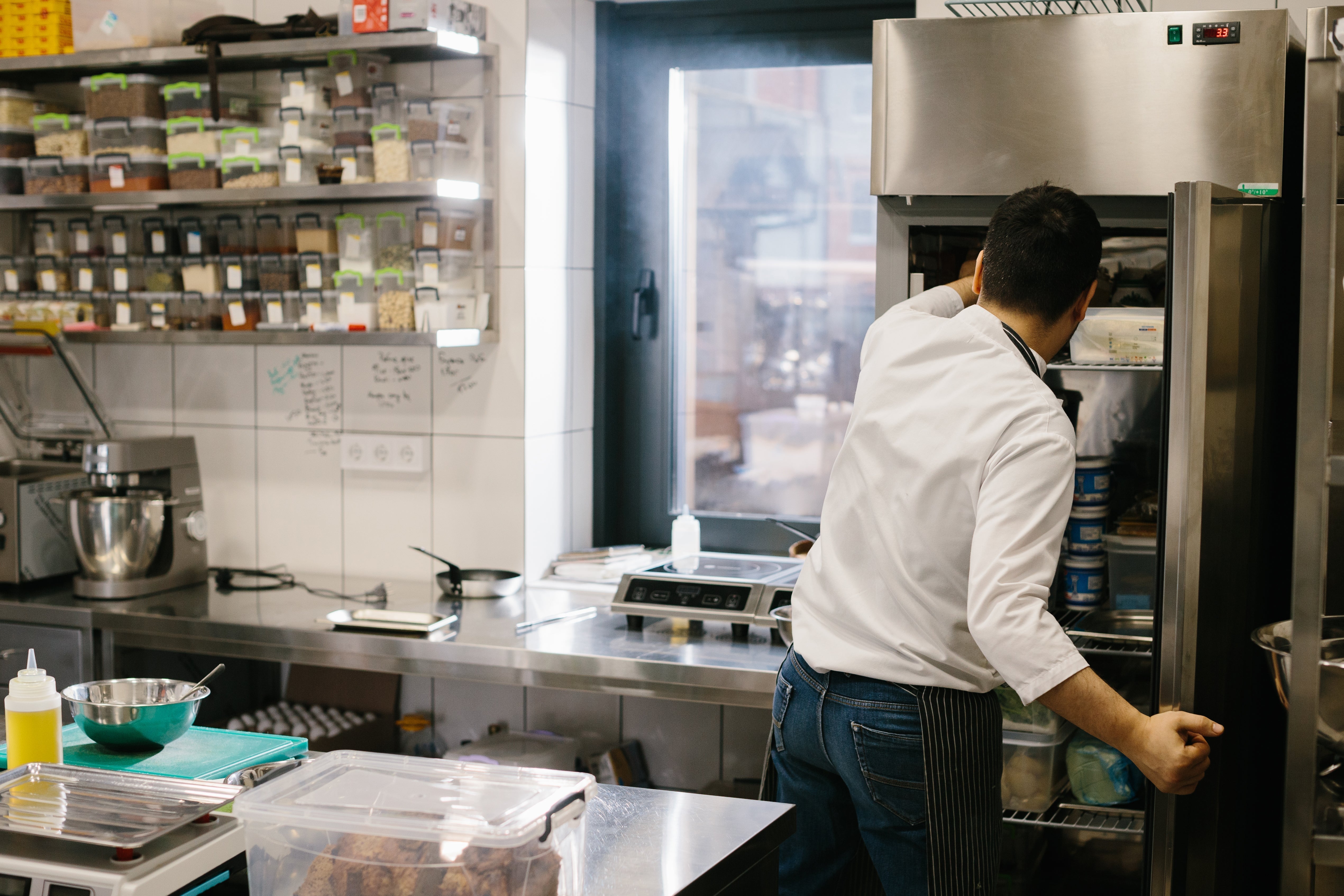 Chef organising ingredients in a commercial refrigeration unit to maintain food safety and reduce waste in a restaurant kitchen.
