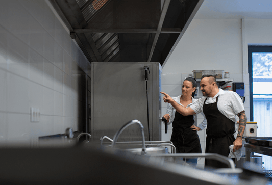 A chef is showing the sous-chef how to use the new combi oven the restaurant owner recently purchased.