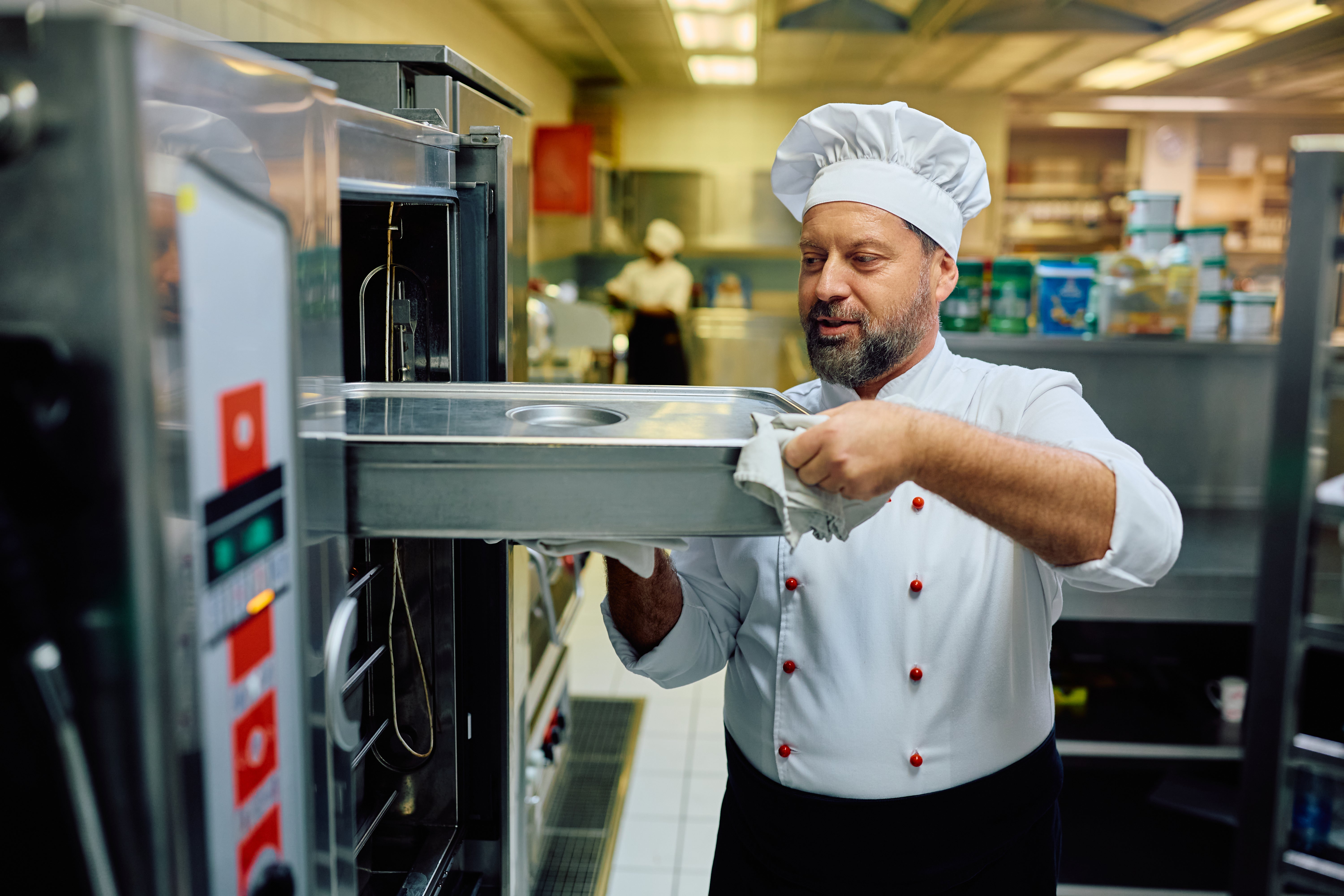 Chef checking commercial oven in restaurant kitchen during commercial kitchen equipment repairs causing operational downtime.